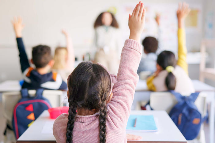 children in a classroom raising hand